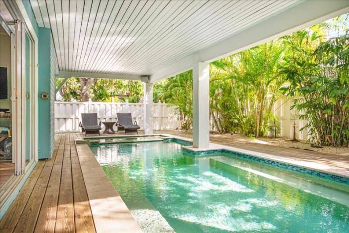 covered pool area with two loungers at far end of the pool with a spa and white privacy fencing in background located on Anna Maria Island