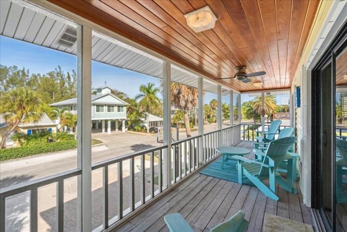screened in balcony with wood floor ceiling overlooking road with basketball goal in driveway and wooden chairs lining the decked area located on Anna Maria Island
