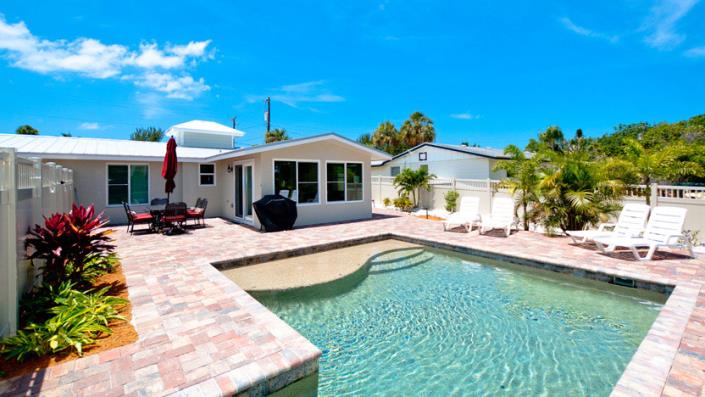backyard featuring pool with baja shelf surrounded paver patio with grill at corner of house and two loungers to the side of the pool located on Anna Maria Island