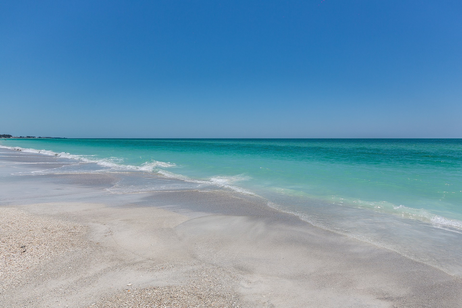 small breaking waves along coastline with turquoise blue water & clear sky along Anna Maria Island