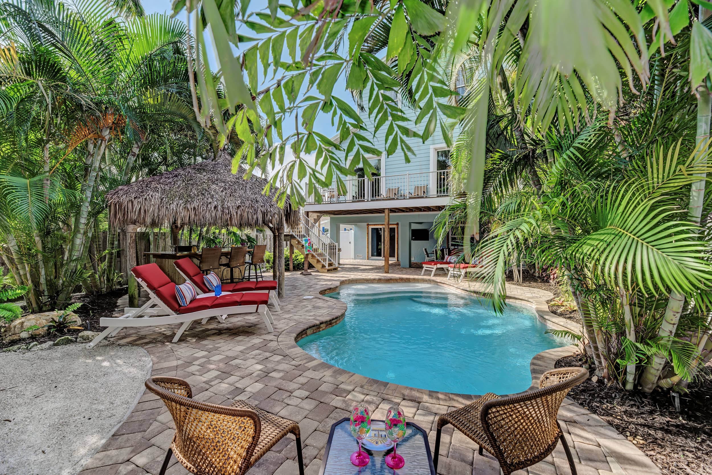 backyard oasis featuring a pool, tiki hut and bar, four loungers around the pool surrounded by tall foliage providing shade and privacy located on Anna Maria Island