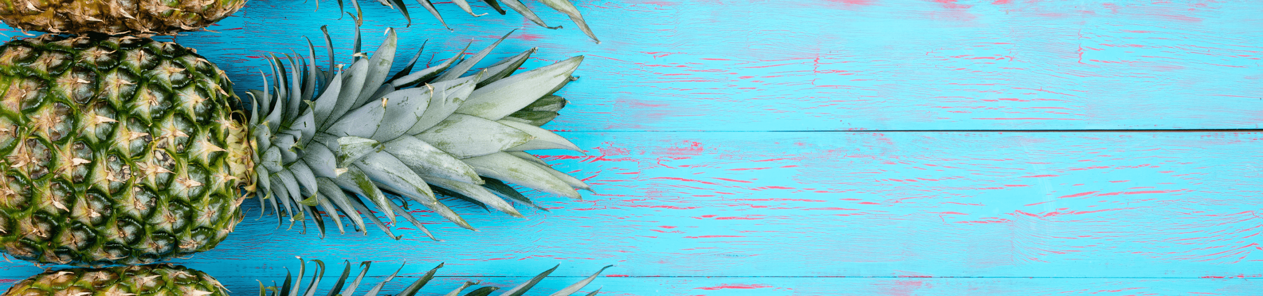 pine apples aligned vertically on the left on a worn wooden deck painted blue with red peeking through