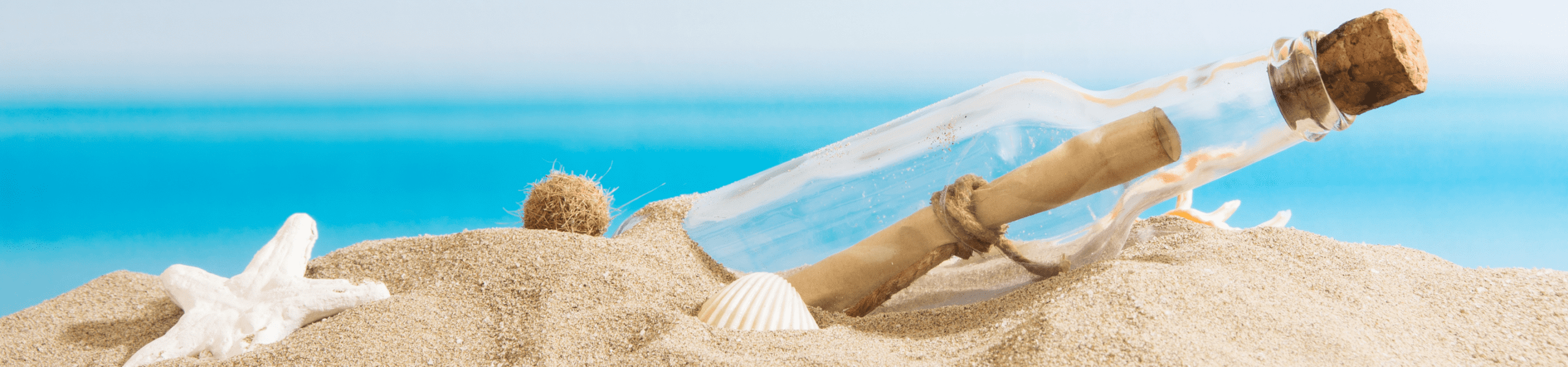 rolled piece of paper tied with string in a corked glass bottle surrounded by a few shells in the sand