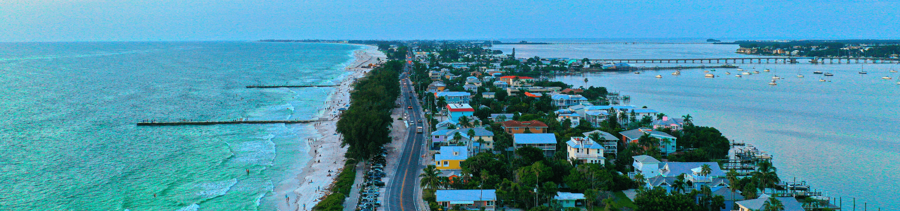 aerial view from drone looking down at Bradenton Beach on Anna Maria Island as the sun begins to set with the Gulf on the left and bay on the right with various houses in the middle of the island