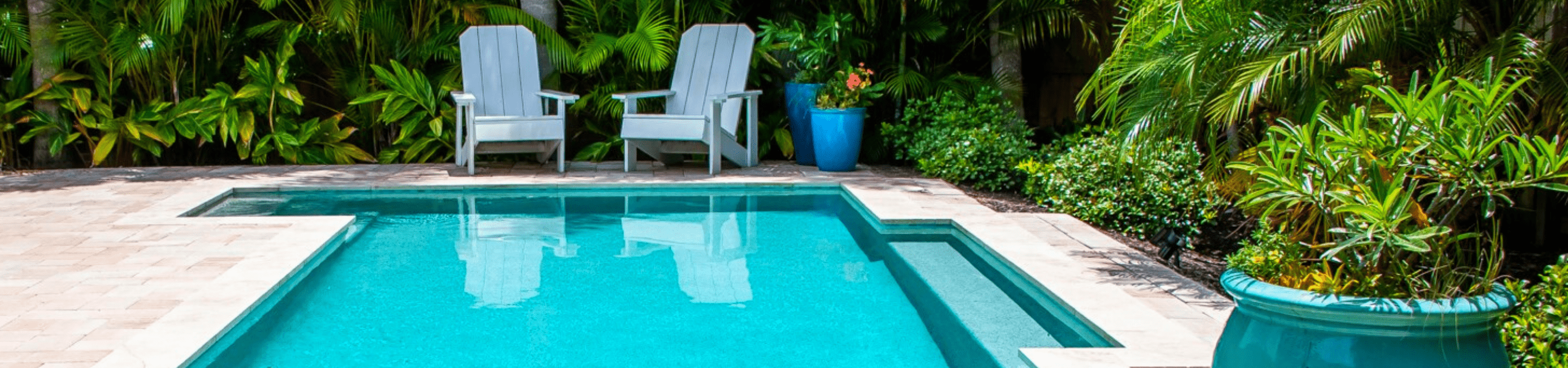 Arectangular pool with two adirondack chairs at the far end of the pool with thick green foliage surrounding the backyard located on Anna Maria Island