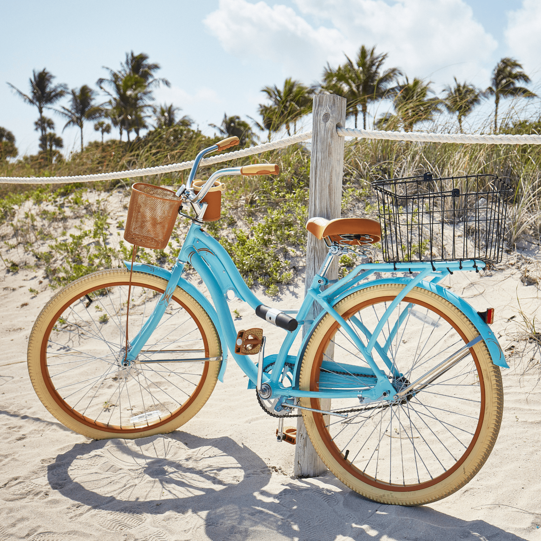 Blue and tan bike on the beach, leaning up against a fence post.