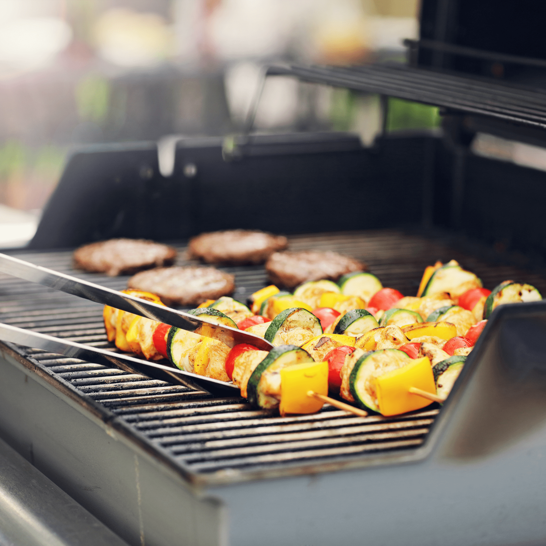 Gas grill with kabobs and hamburgers cooking.