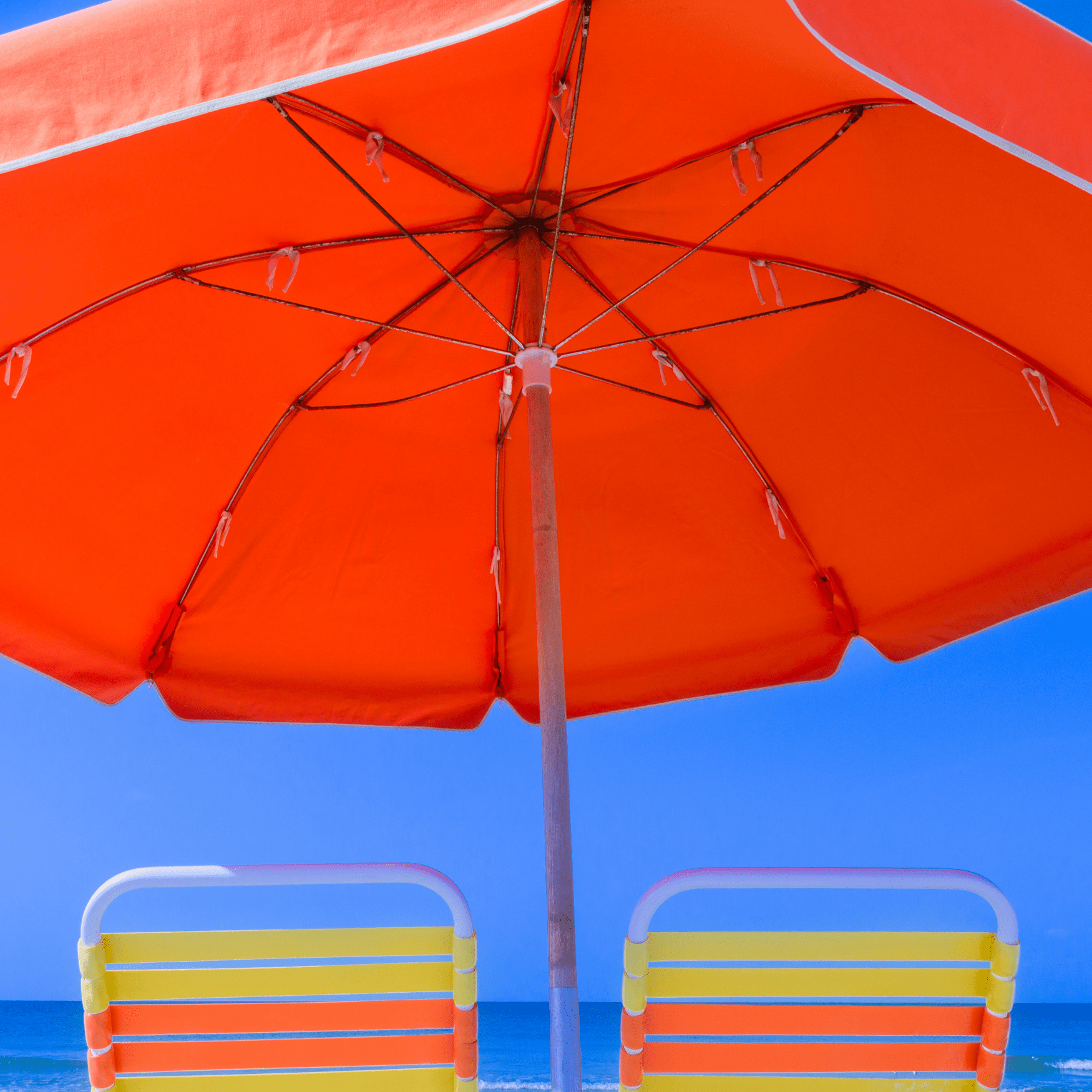 Orange umbrella and two beach chairs on the beach.