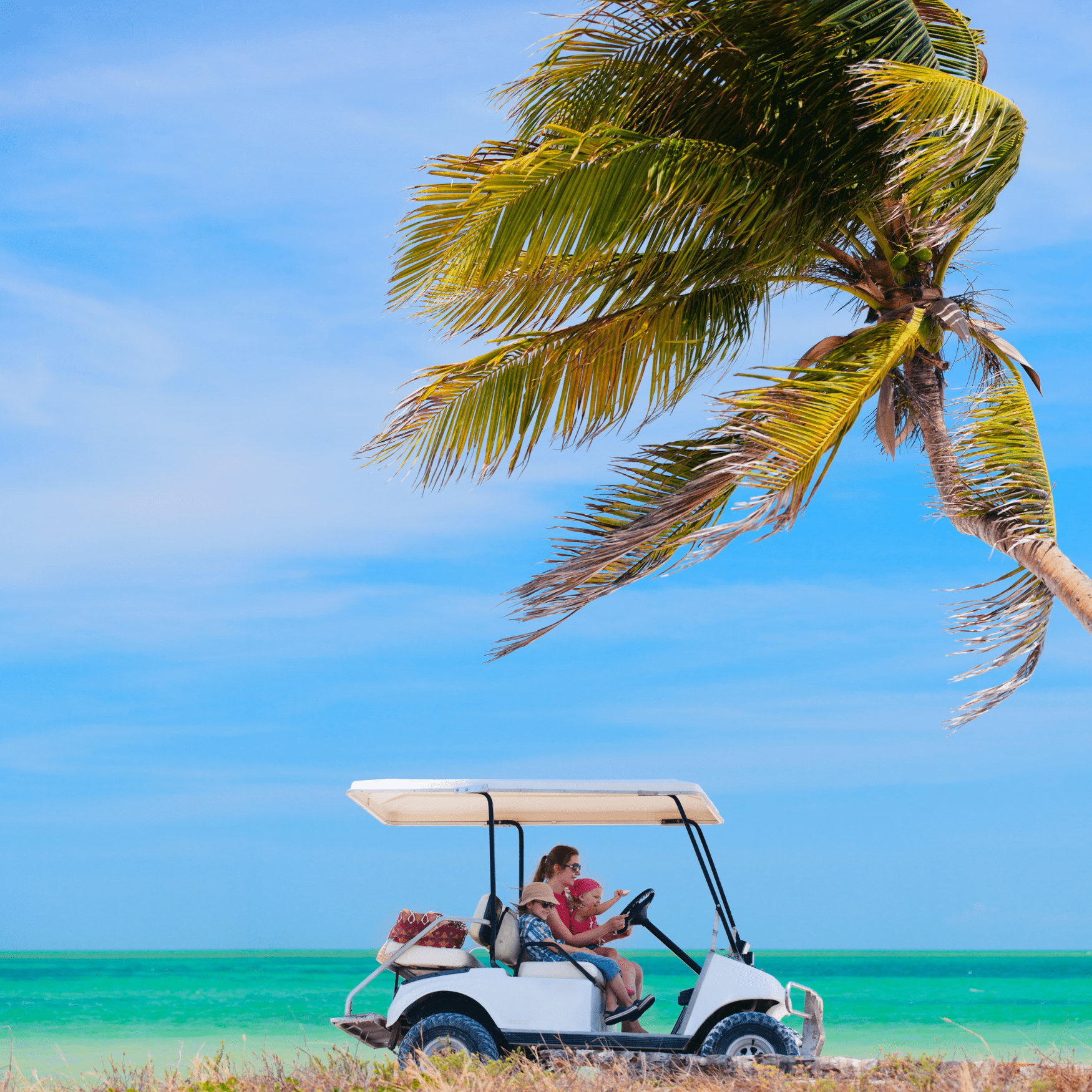 lady sitting in covered golf cart with a little boy as the passenger and baby girl in her lap with the gulf of Mexico in the background