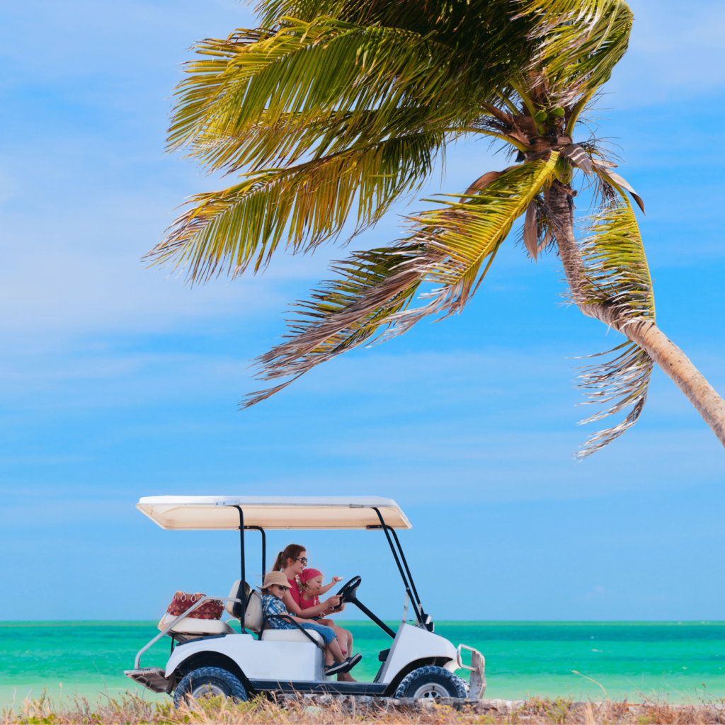 Woman driving a golf cart on the beach with two children.