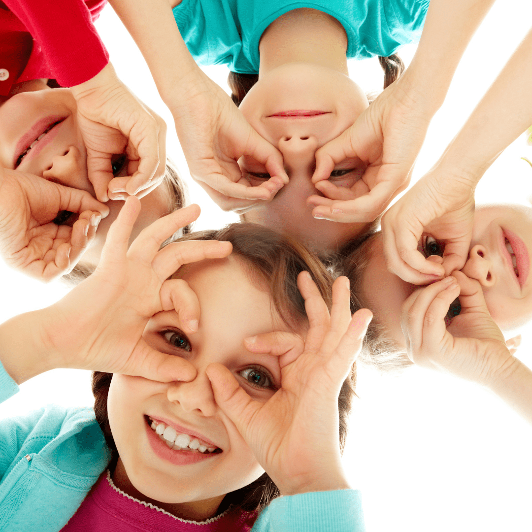 Four children making binoculars around their eyes with their hands.