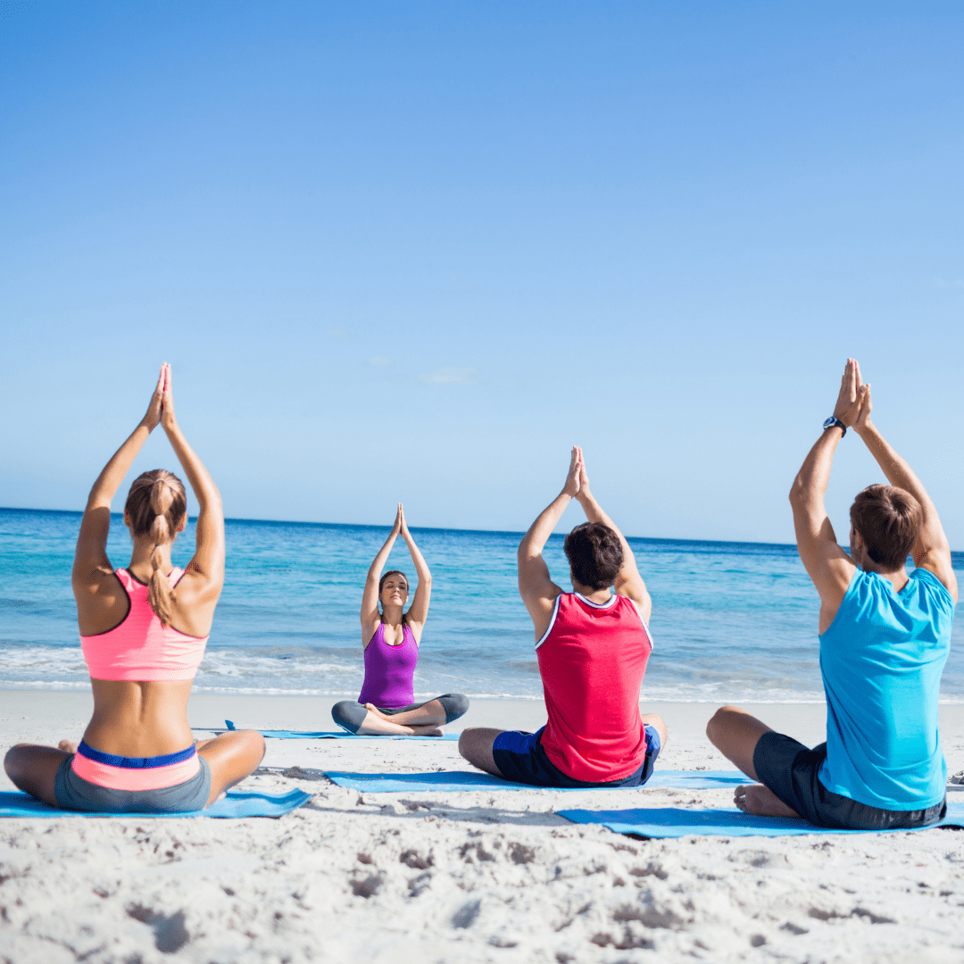 Four People sitting in yoga poses on the beach.
