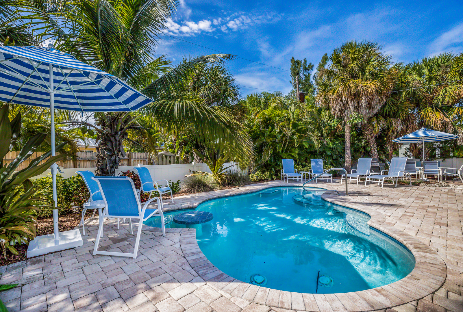 The Backyard pool and pool deck with blue lawn chairs and a blue and white umbrella at Toes in the Water by Anna Maria Life Vacation Rentals