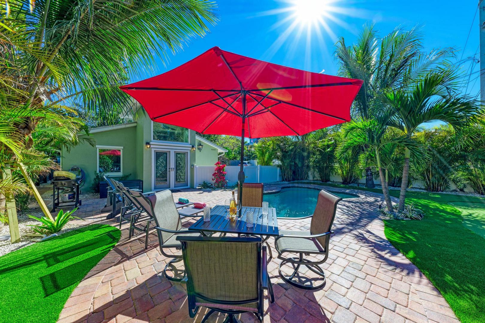 Outdoor dining table with red umbrella beside the pool at Turtle Tyme, a vacation rental by Anna Maria Life Vacation Rentals