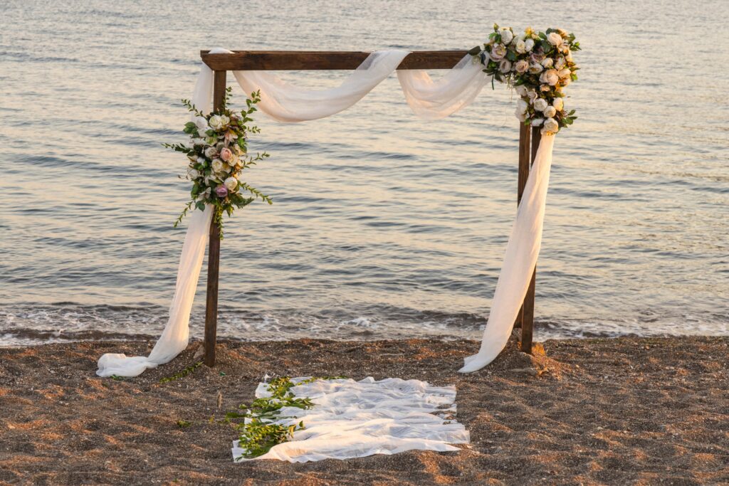 Beachfront wedding arch with flowing fabric and flowers on sand at Anna Maria Island Life Vacations.