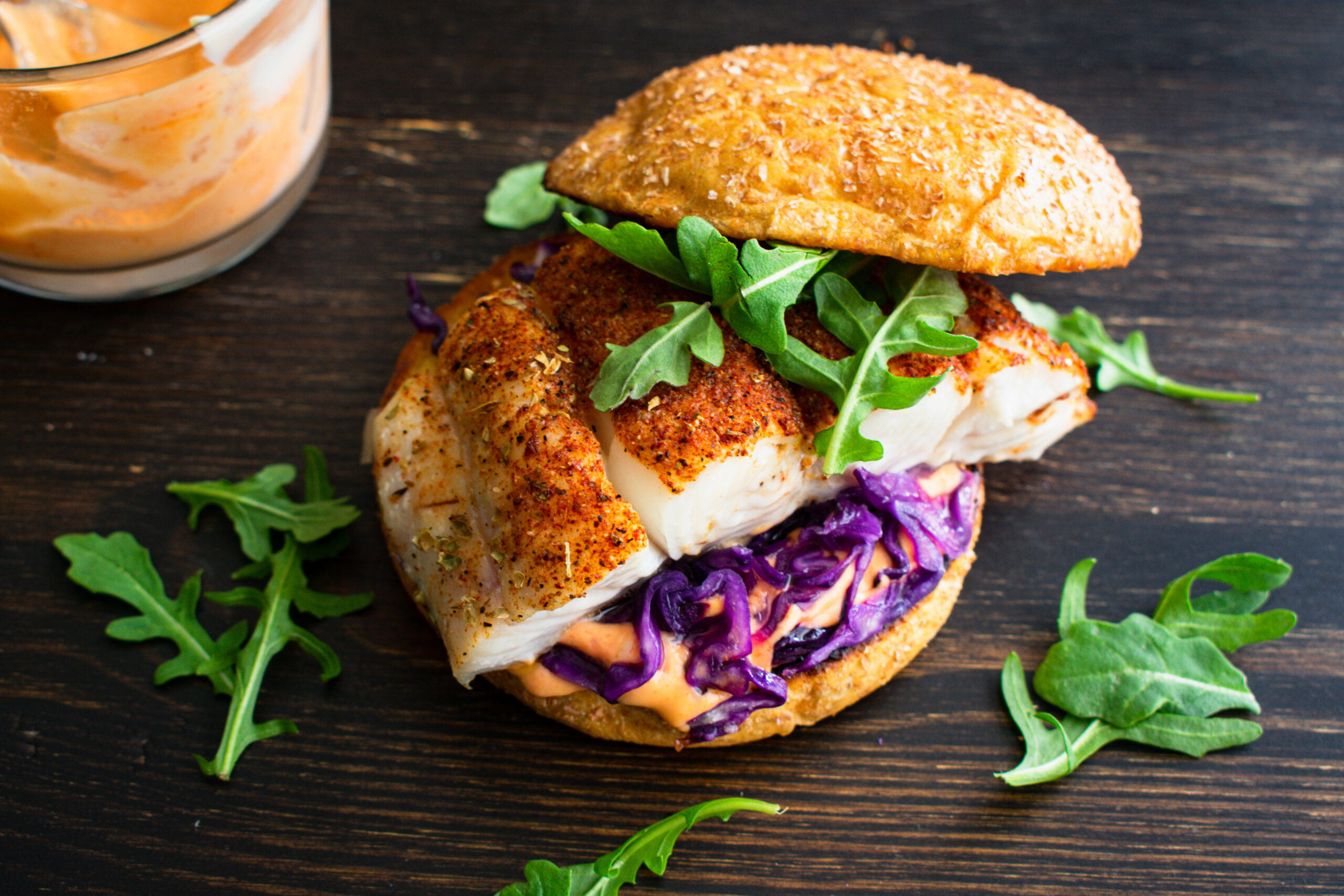 Blackened Fish Burger and Sriracha Mayo: A halibut fish sandwich with red cabbage and arugula on a whole wheat brioche bun