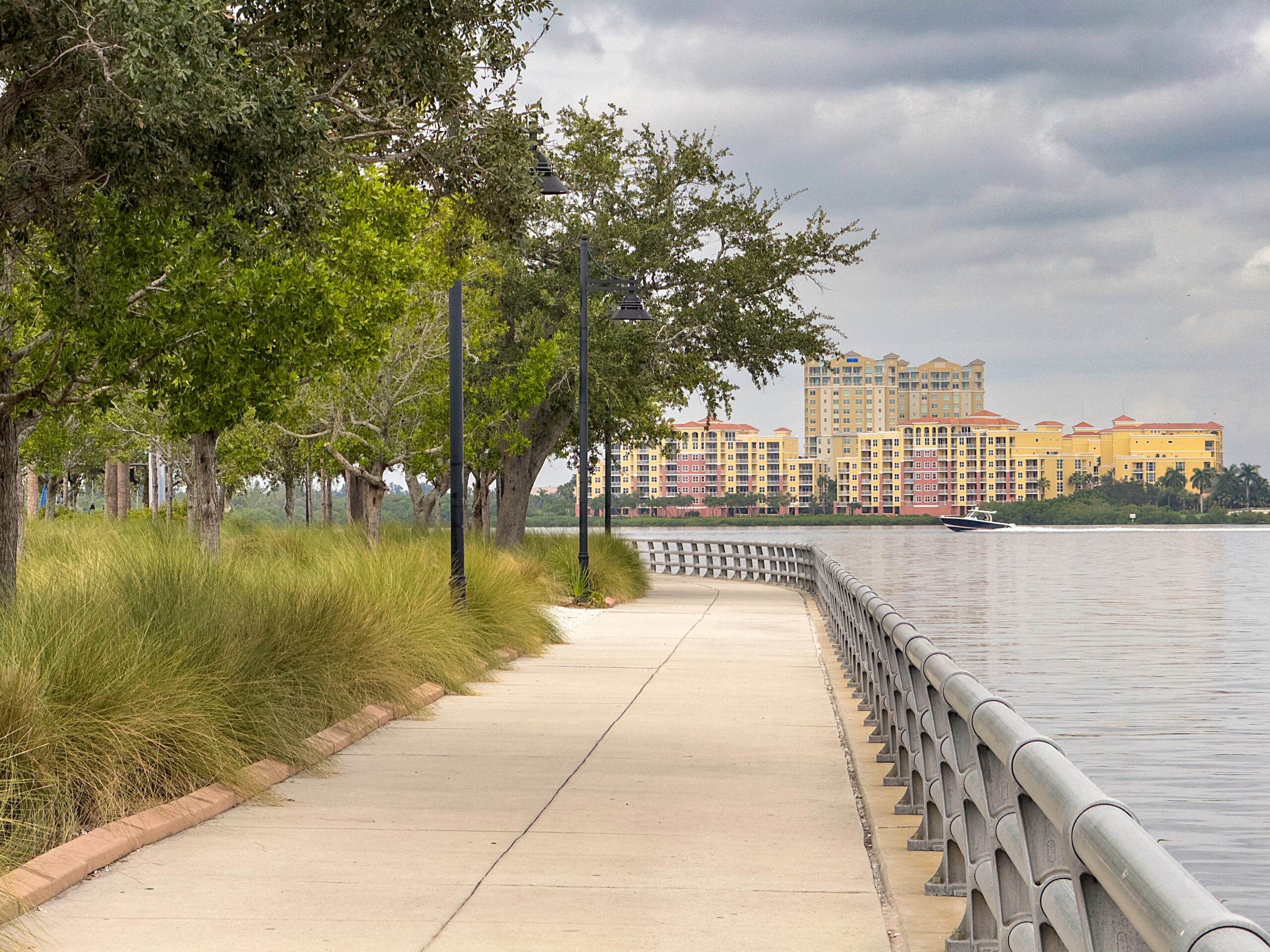 Perspective of municipal riverwalk in Bradenton, Florida, with view of speedboat passing by condominiums along Manatee River, on a cloudy afternoon 